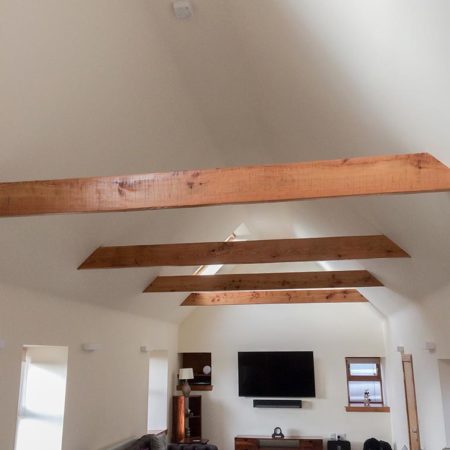 Wooden roof trusses in view in a lounge area with sofa, coffee table and tv