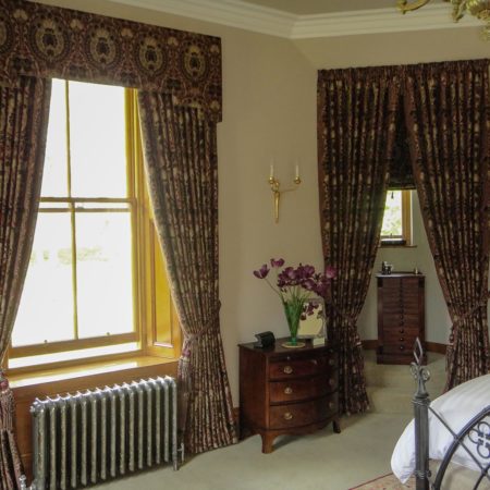 Stately bedroom showing large window with traditional style curtains and edge of bed