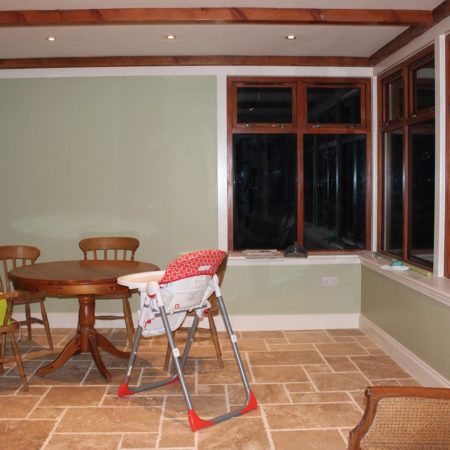 Conservatory area with floor tiles, large high windows nad a dining table, chairs and highchair