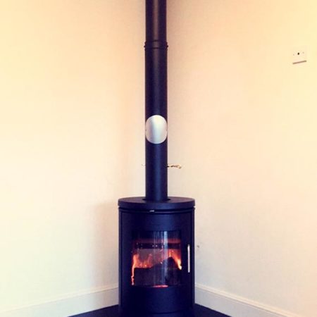 Black wood burner and flue to ceiling positioned in corner of a room