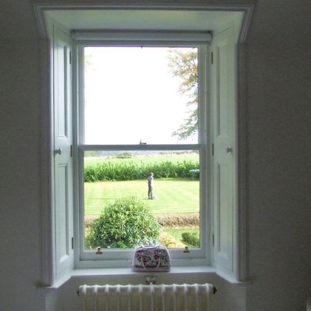 Inside of room looking towards traditional window with wooden shutters and garden scene through the window panes