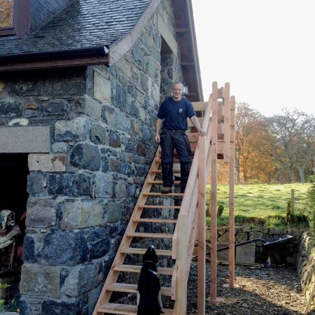Wooden staircase built at gable end of stone build garage for access to upper level