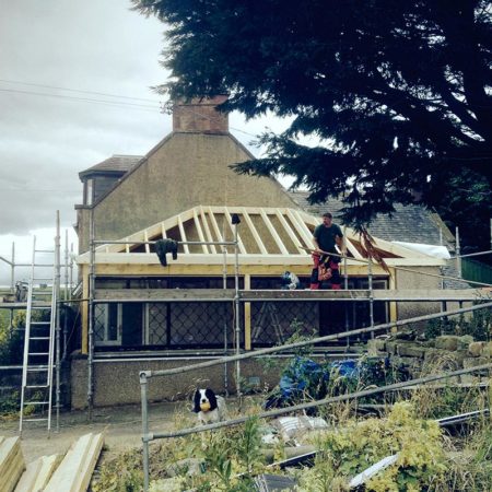 Gable end of house with extension part built on to gable end showing roof timbers being added