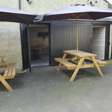 Two picnic benches with sun parasols in courtyard of Market Arms in Banff
